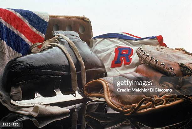 The skate, jersey, trapper, and blocker of Canadian professional hockey player Eddie Giacomin, goaltender for the New York Rangers, on a reflective...