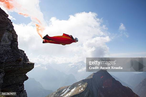 wingsuit flier launches at cliff edge, smoke trail - herausforderung stock-fotos und bilder
