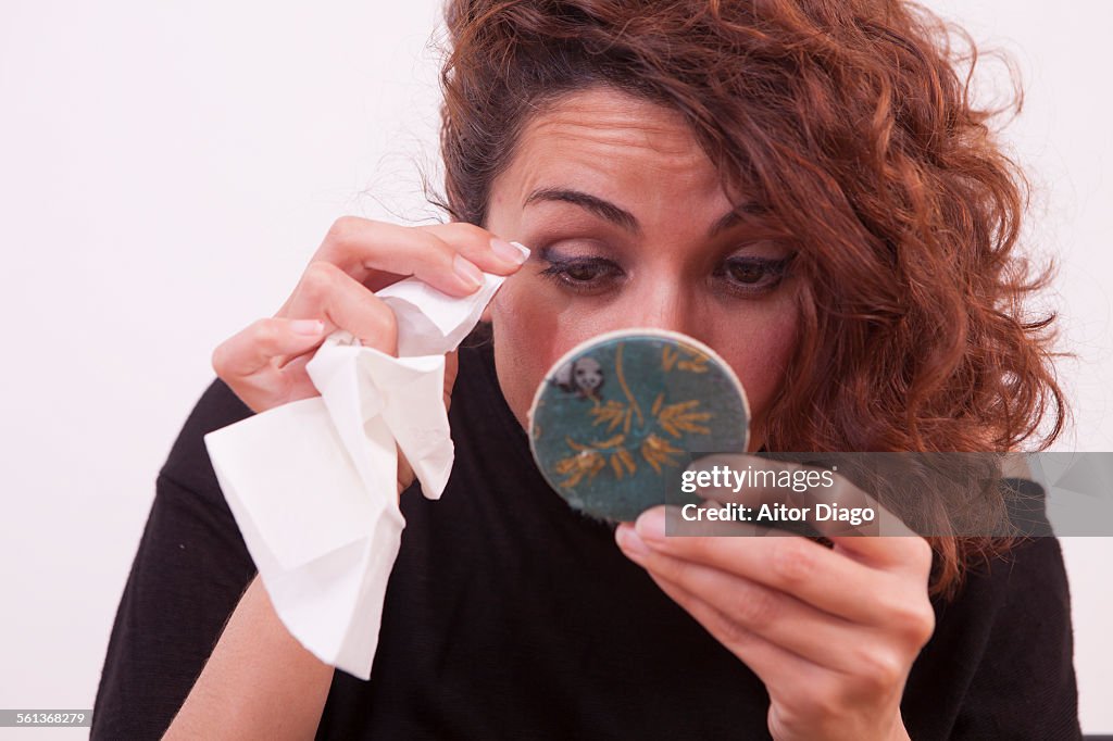 Woman removing eye makeup in mirror with a tissue