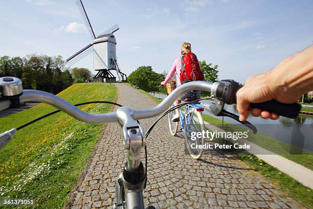 couple riding bikes towards windmill. - bruges photos et images de collection