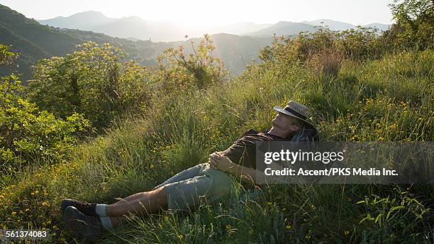 hiker relaxes in meadow, hat pulled over face - green hat stock pictures, royalty-free photos & images