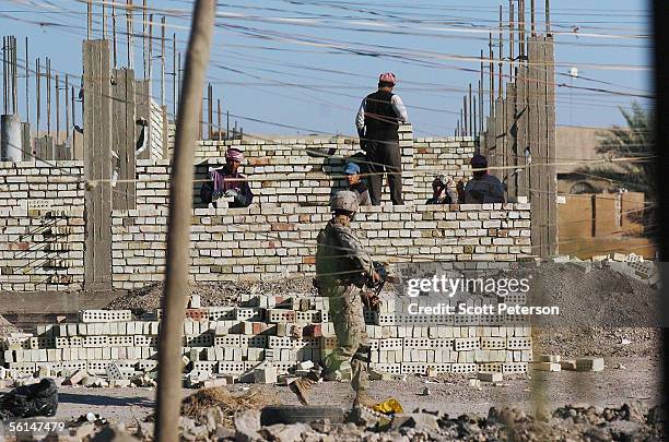 Marine of Fox Company, 2nd Battalion 6th Marine Regiment, patrols past men reconstructing of a building November 12, 2005 in Fallujah, Iraq. One year...