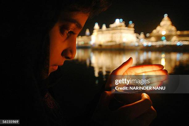 An Indian Sikh devotee lights an earthen lamp in front of the illuminated Golden Temple in Amritsar, 14 November 2005, the eve of the 536th birth...