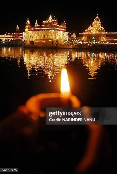 An Indian Sikh devotee holds an earthen lamp in front of the illuminated Golden Temple in Amritsar, 14 November 2005, the eve of the 536th birth...