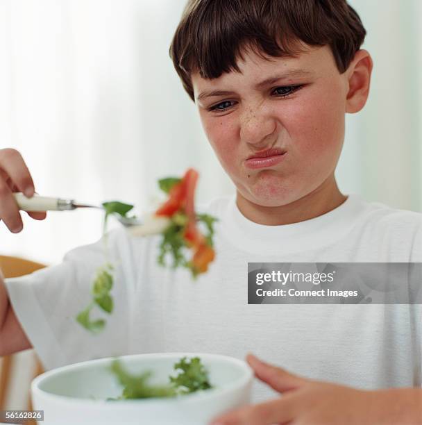 boy looking disgusted at salad - grimace de crispation photos et images de collection