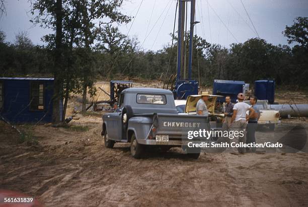 Oil field workers AKA roughnecks, with drilling rig truck and Chevrolet pickup truck, drilling an oil well, Texas, 1954.