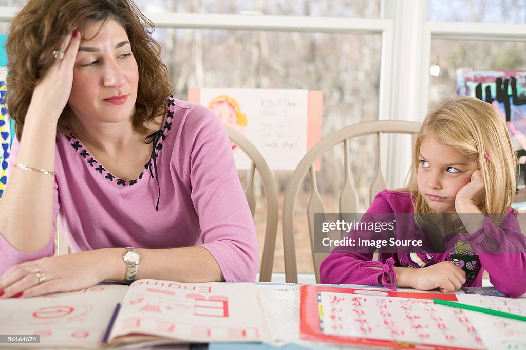 Frustrated mother helping bored daughter with homework