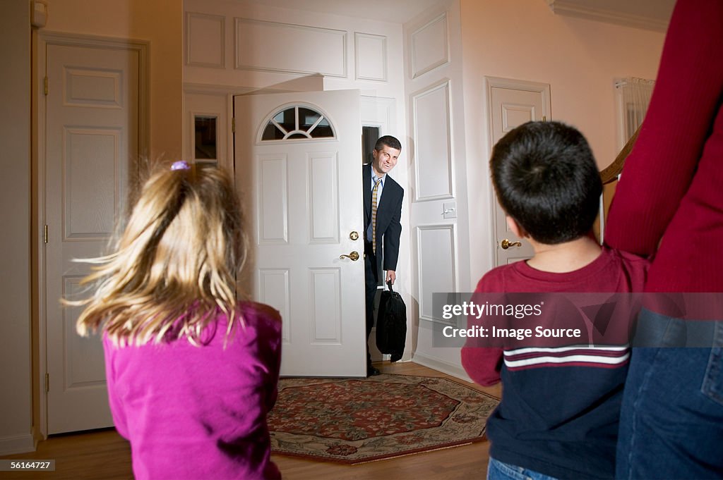 Family greeting businessman as he arrives home