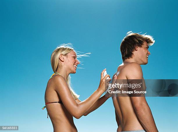 frau sprühen sun creme auf boyfriend's back - suntan lotion stock-fotos und bilder
