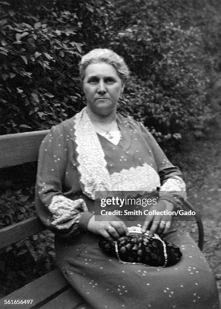 An elderly woman in smart clothes with a handbag, seated on a park bench, Germany, 1950.