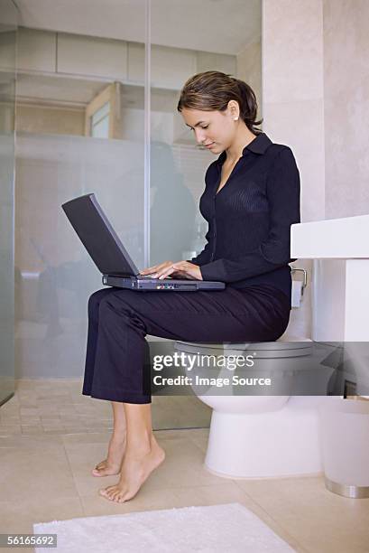 woman sitting on a toilet using laptop computer - woman sitting on toilet stock-fotos und bilder