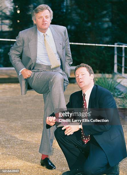 Scottish comedian and impressionist Rory Bremner polishes the shoes of British businessman Michael Grade, CEO of Channel 4, UK, circa 1993.