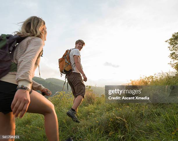 hiking couple set off across hillside meadow - bergwandeling stockfoto's en -beelden