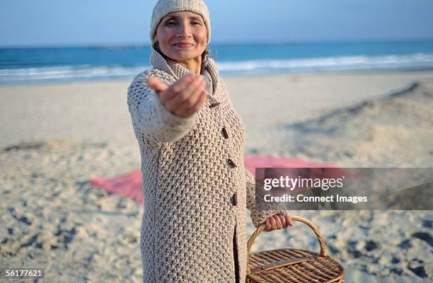 senior woman holding picnic basket and beckoning - heranlocken stock-fotos und bilder