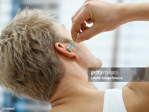 man putting cotton bud in his ear - human ear stockfoto's en -beelden