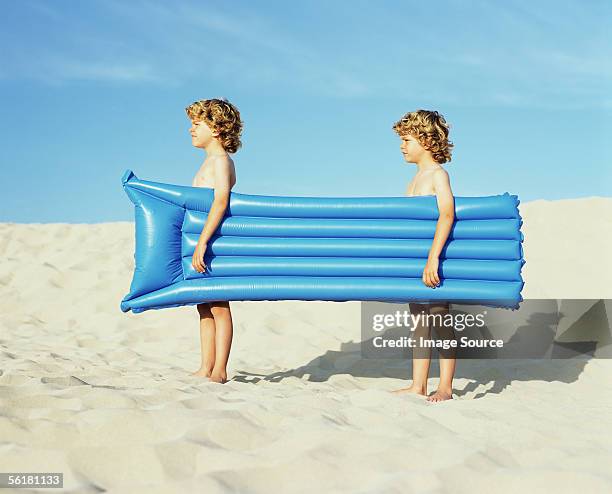 twin boys carrying an inflatable - tweeling stockfoto's en -beelden