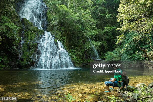 father with baby relaxing by waterfall in forest - amami stockfoto's en -beelden