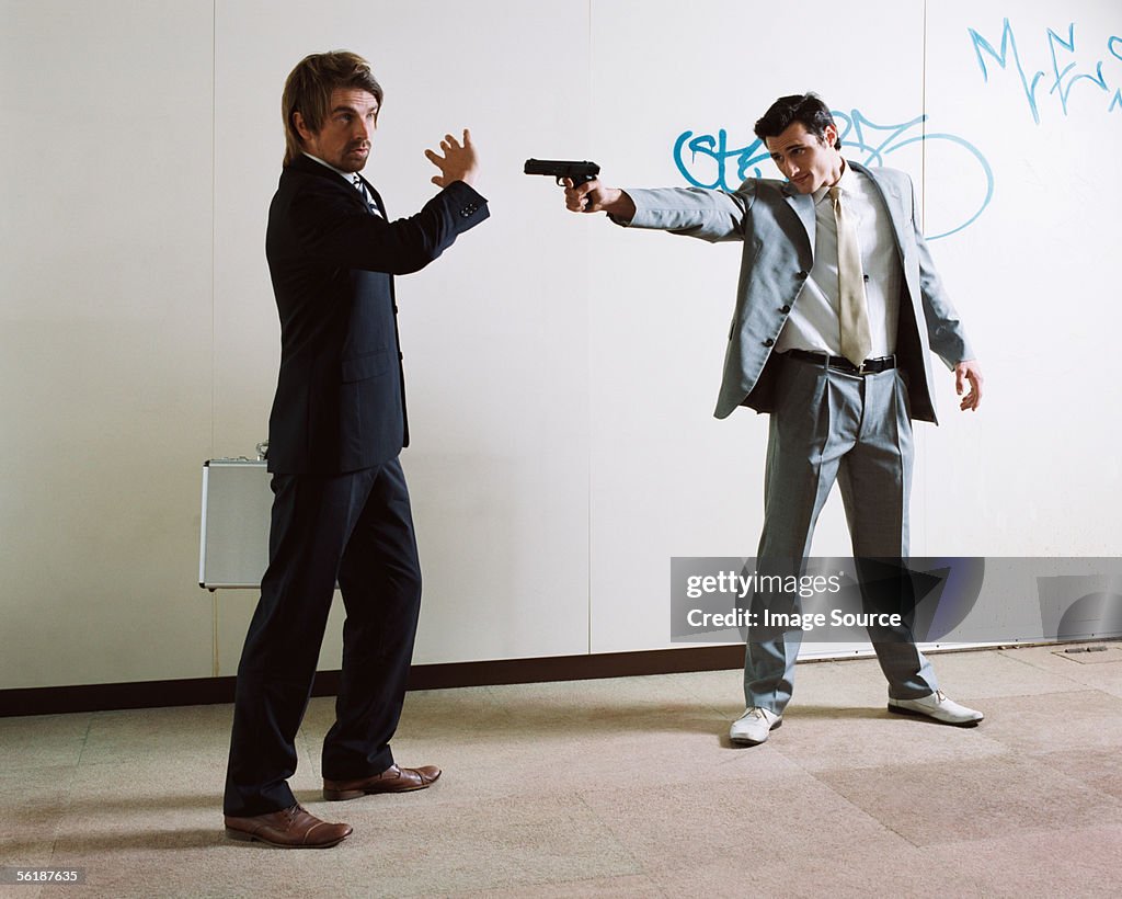 Businessman pointing a gun at colleague