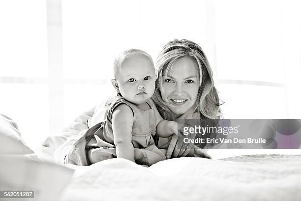 mother and baby girl laying on a bed together look - eric van den brulle stock pictures, royalty-free photos & images