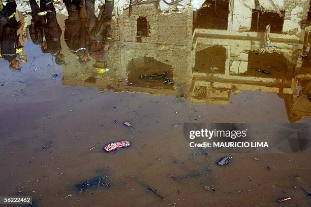 Sandal of a child appears floating in a huge puddle of water as members of Iraqi civil defense are reflected with destroyed building at the site...