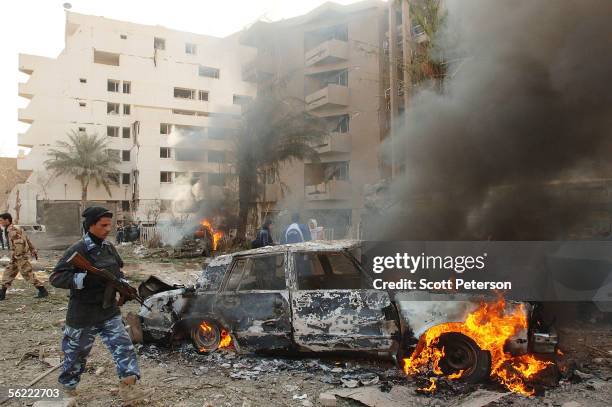 An Iraqi policeman walks by a burning car in the aftermath of a double suicide car bomb attack that struck civilians living near the blast walls that...