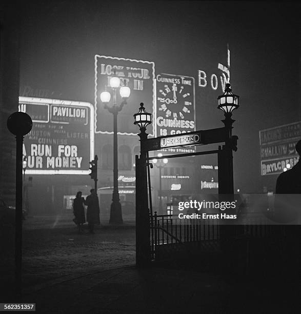 Couple walking in Piccadilly Circus at night, London, circa 1953.