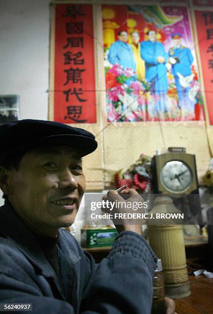 Wang Hemin smokes a cigarette in his home, decorated witha poster of Communist China's former top leaders Mao Zedong, Zhou Enlai, Chu De and Liu...