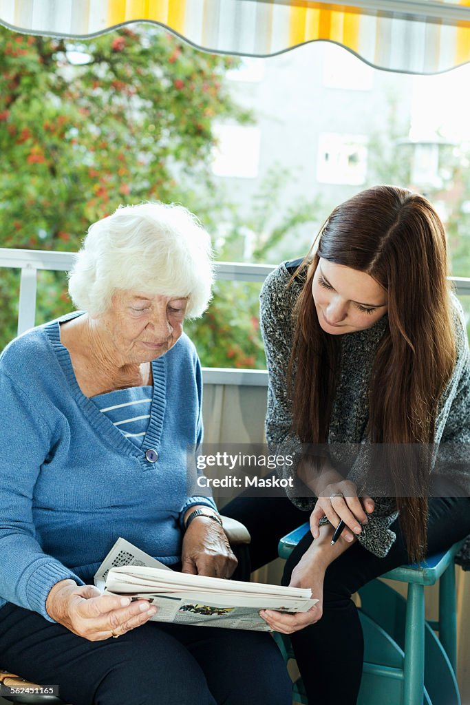 Grandmother and granddaughter reading newspaper on porch