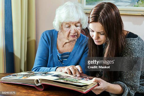 grandmother and granddaughter looking at photo album in house - granddaughter stockfoto's en -beelden