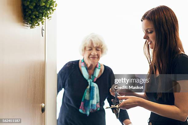 elderly woman looking at granddaughter unlocking front door of house - generationsunterschied stock-fotos und bilder