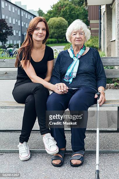 portrait of smiling woman sitting with granddaughter on bench outdoors - grandma cane stock pictures, royalty-free photos & images
