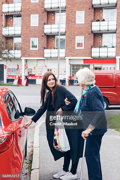young woman opening car door for grandmother on city street - grandma cane stock pictures, royalty-free photos & images