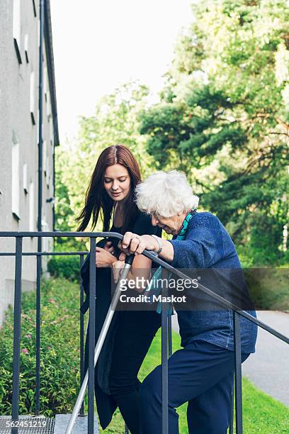 young woman helping grandmother to climb steps outdoors - grandma cane stock pictures, royalty-free photos & images