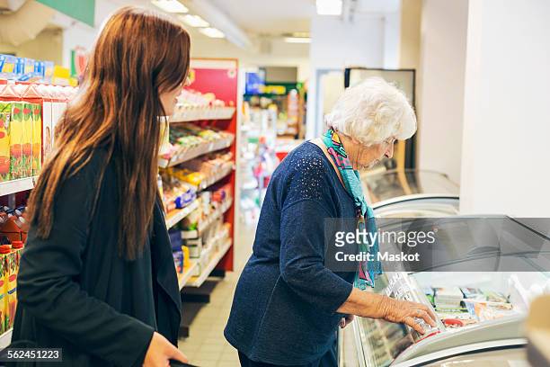 young woman looking at grandmother shopping in supermarket - client carer stock-fotos und bilder