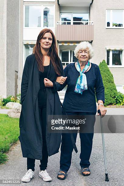 full length portrait of young woman standing with grandmother outside house - grandma cane stock pictures, royalty-free photos & images
