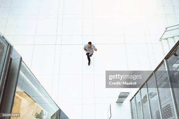 high angle view of businessman using mobile phone while walking in modern office - long shot stock pictures, royalty-free photos & images