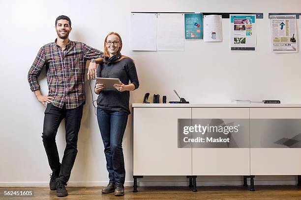 full length portrait of smiling business colleagues standing by sideboard in creative office - woman standing full length stock pictures, royalty-free photos & images