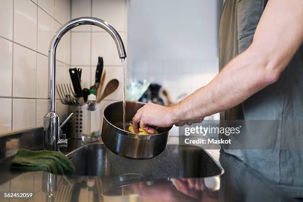 midsection of man washing sauce pan with scouring pad at sink - brillos stockfoto's en -beelden