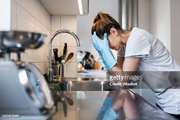 side view of tensed woman leaning at sink in kitchen - frau putzen stock-fotos und bilder