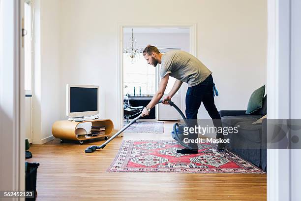 side view of man vacuuming hardwood floor - vacuum cleaner stock pictures, royalty-free photos & images
