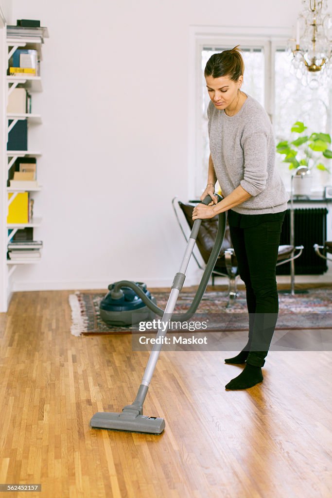 Woman vacuuming hardwood floor at home