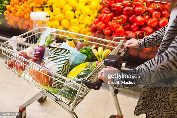 midsection of woman pushing groceries in shopping cart at supermarket - empujar fotografías e imágenes de stock