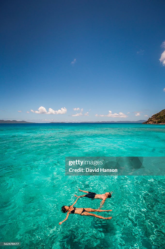 BRITISH VIRGIN ISLANDS, CARIBBEAN. A couple float on their backs in clear teal Caribbean water.