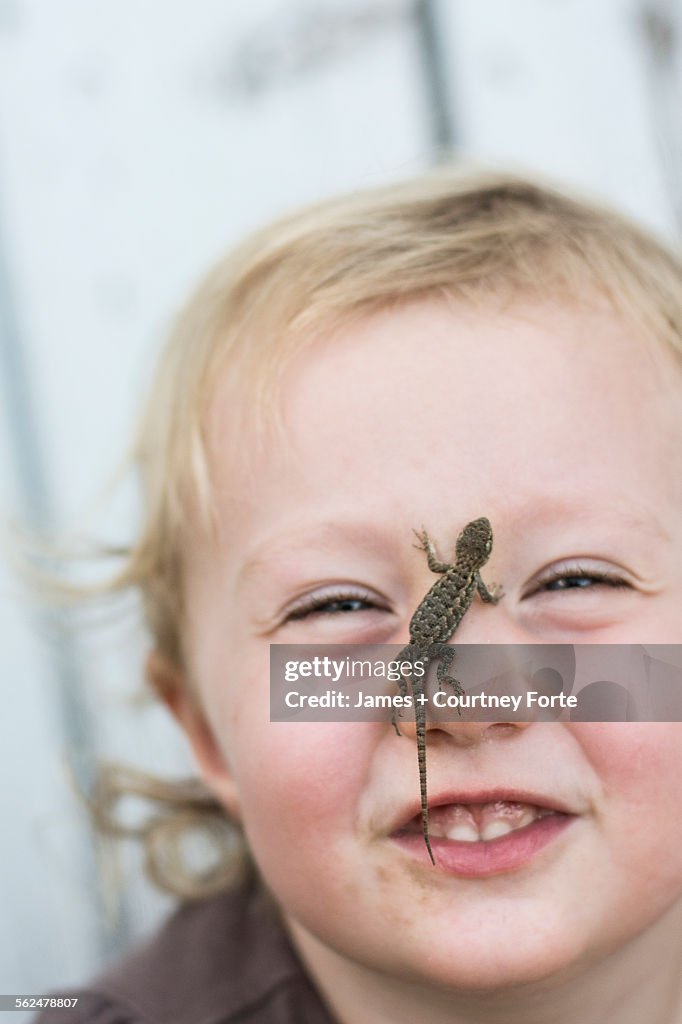 Toddler girl smiles at camera with Sagebrush lizard on nose in Chico, California.