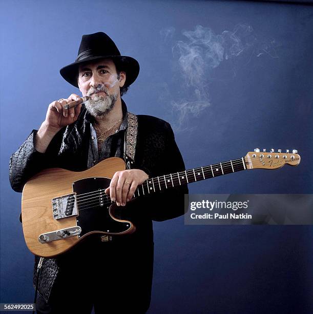 Studio portrait of American Blues musician Roy Buchanan as he poses, with his guitar, and smokes a cigar, Chicago, Illinois, April 15, 1985.