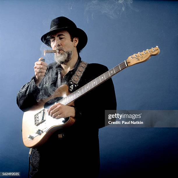 Studio portrait of American Blues musician Roy Buchanan as he poses, with his guitar, and lights a cigar, Chicago, Illinois, April 15, 1985.