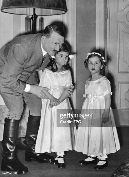 Genocidal German dictator and Nazi leader Adolf Hitler adjusts the arms of one of Joseph Goebbels' daughters as they and another Goebbels daughter...