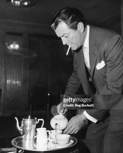 Actor Robert Taylor pouring himself a cup of tea, with a cigarette in his mouth, at a press reception for his new film 'Adamson of Africa', at the...