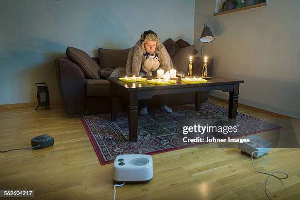 man sitting in cold living room - cold temperature fotografías e imágenes de stock
