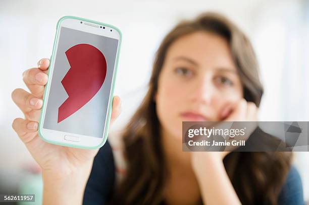 woman showing image of broken heart on her smartphone - breaking up stock pictures, royalty-free photos & images